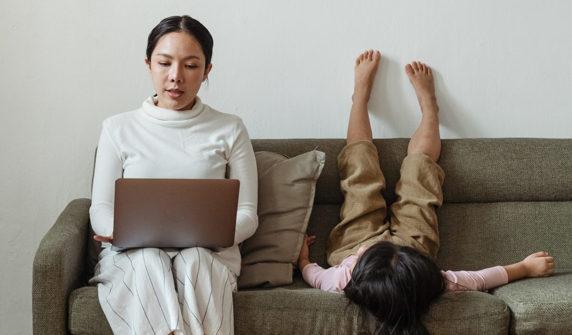Woman working on laptop with child acting silly on the couch